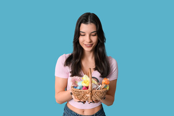 Pretty young woman holding wicker Easter basket with cosmetics on blue background