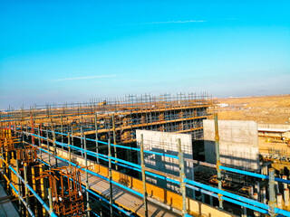 A construction site with scaffolding and a blue sky in the background. Scene is one of progress and hard work