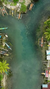 Tropical forest and Bogac Cold Spring in Surigao del Sur. Fishermens houses and boats over the water. Philippines. Vertical view.