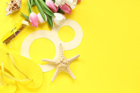 Composition with paper figure 8, beach accessories and tulip flowers for International Women's Day on yellow background