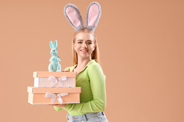 Young girl with Easter bunny ears, toy rabbit and gifts on beige background