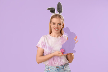 Young girl with Easter bunny ears and paper rabbit on lilac background