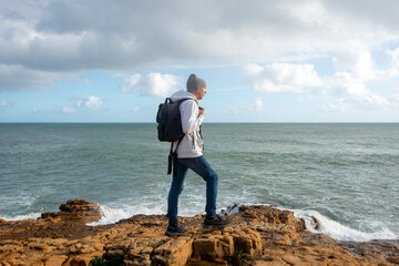Man, hiker standing on rocks by the ocean looking at the view. - obrazy, fototapety, plakaty
