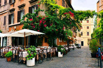 Beautiful ancient street in Rome lined with leafy vines, flowers and restaurant tables, Italy