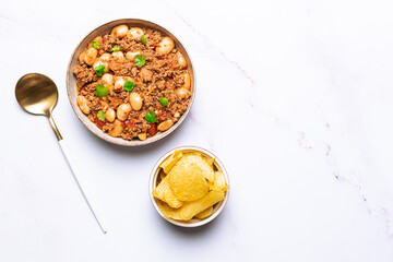 Tasty homemade chili con carne with chips on the wooden tray on white marble table top view.
