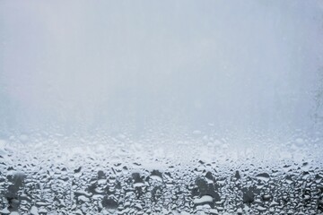 Beschlagene feuchte Glasscheibe mit Wassertropfenmuster vor grau-weißem Hintergrund bei Frost und...