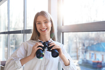 Young woman with binoculars near window at home