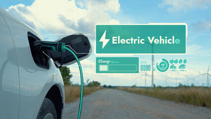 Electric car recharging energy from EV charging station display futuristic smart battery status hologram by EV charger plug cable in wind turbine farm. Alternative clean energy sustainability. Peruse
