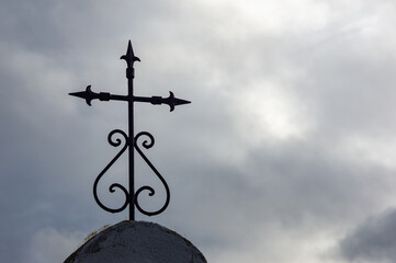 Celestial Contrast: ancient forged iron Christian cross, against a cloudy sky.