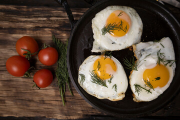 Fried eggs in a pan with vegetables and herbs on a black background.