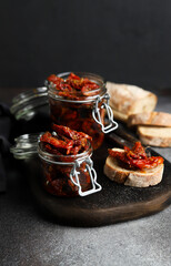 Sun-dried tomatoes in a glass jar. Tomatoes with spices. Dark background. Summer dish. Italian cuisine. Sun-dried tomatoes on white bread.