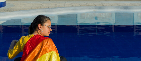 joven mujer sentada al lado de la piscina en la tarde con la bandera del orgullo gay casual 