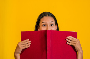foto de estudio de joven mujer con un libro tapando parte de su cara y mirando la cámara