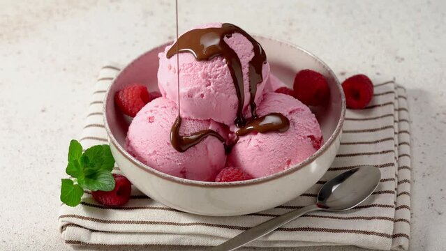 Pouring chocolate sauce over raspberry ice cream scoops