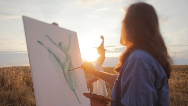 Man holding brush and palette while painting on canvas and looking at dancing female in light of sunset. Adorable woman in white gown making elegant movements to inspire artist in middle of nature.