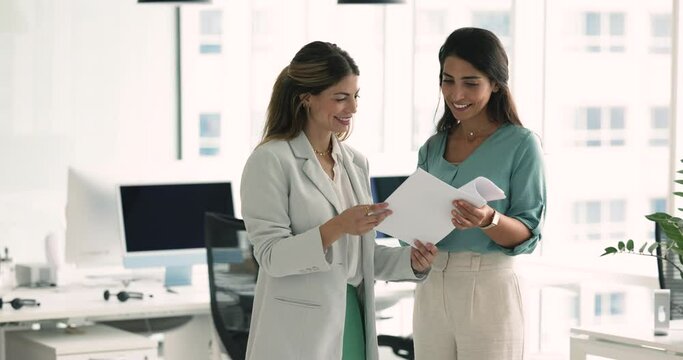 Two young attractive Latina businessladies met in company office review contract details, share opinions, make agreement, accomplish formal meeting with shake hands. Business, consultation, teamwork