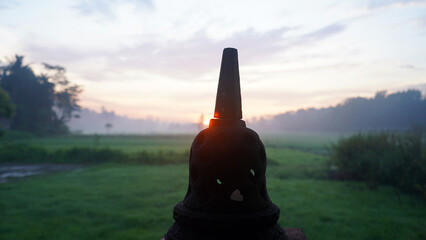 Morning view of the sunrise over the field with small temple stone exterior as foreground. Buddha...