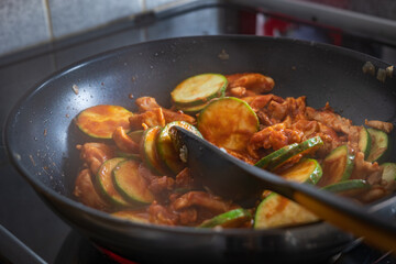 Frying chicken fillet slices with courgette and onion in frying pan for enchilada filling