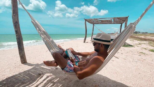 Man reading a book in hammock on the beach, La Guajira, Colombia