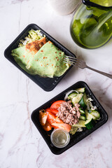Green salad with tuna, cucumbers, tomatoes and cabbage with green thin pancakes of spinach in plastic boxes.