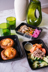 Rice noodles with chicken, carrots, peas, green beans, corn and sesame seeds with green salad with tuna and buns with cheese and onions in plastic boxes.