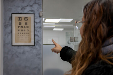 Smiling young woman checking up vision at optician clinic. Cute female choosing glasses at optics...