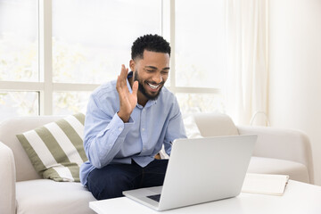 Happy African American student guy enjoying online conversation at laptop, waving hand hello, smiling, laughing, using Internet technology connection for education, teaching, communication on Internet