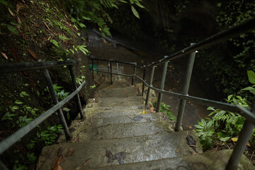 Moss-covered stairs lead to a mountain crevice with a waterfall in the jungle on the popular tourist island of Bali.