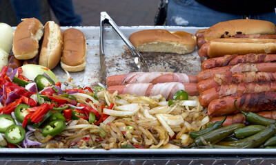 Street vendor cooking bacon wrapped hot dogs, tongs turning food. Popular cuisine for street fairs...