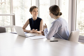 Two young pretty female colleagues talking met in modern boardroom, client and company...