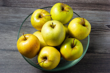 Closeup of golden apples in a glass bowl on wooden background.