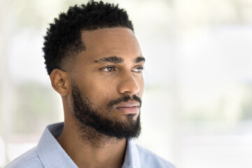Serious handsome young African man indoor casual portrait. Thoughtful dreamy barber model, Black guy with stylish beard posing indoors, looking away in deep thoughts. Close up shot