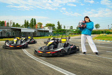 young girl racer with a helmet in her hands near a racing kart