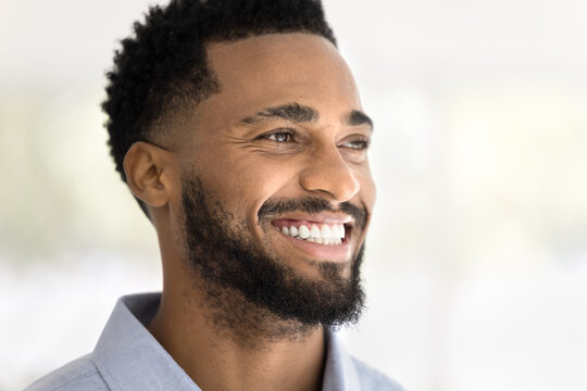 Face of happy attractive young African American man looking away with perfect toothy smile, thinking, promoting dental care, stomatology service. Cheerful handsome Black guy close up portrait
