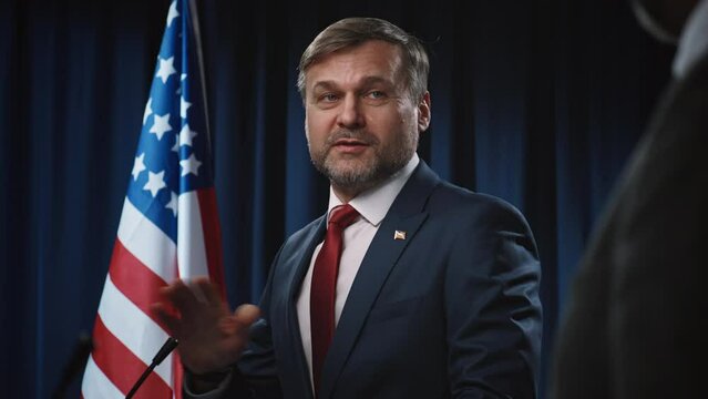 Medium shot of mature Caucasian male candidate running for US Senate delivering his program for fighting inflation and economic crisis, anonymous debate opponent interrupting and contradicting claims