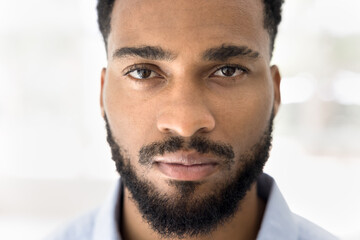 Face close up shot of serious handsome young African man with stylish beard looking at camera....