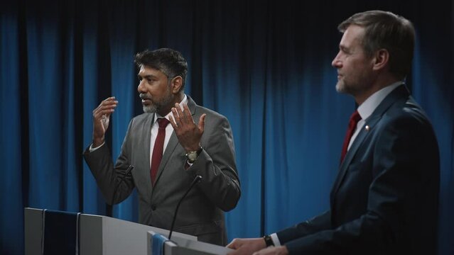 Medium footage of mature Indian male government official in formal suit, tie taking off glasses and categorically denying Caucasian opponents claims, while debating in public during election campaign