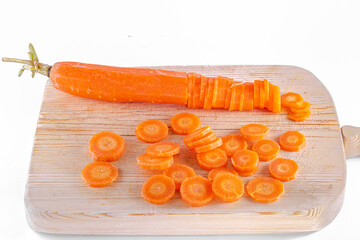 A carrot cut lengthwise and sliced, pieces scattered on a wooden chopping board. Isolated on a white background studio shot high quality image close-up macrophotograph. Oblique overhead view.