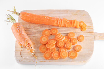Two carrots, one part of it sliced and pieces scattered on a wooden chopping board. Isolated on a...