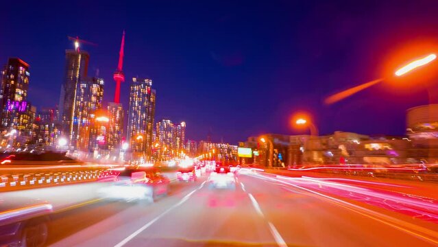 Bright long exposure motion hyperlapse of a speed driving in Toronto, Ontario, Canada. Speedy car front POV view at the highway with a lot of traffic lights stricks. Passing by city downtown buildings