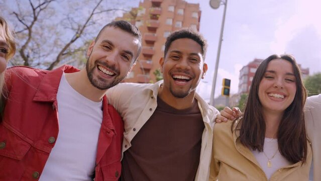 Group of multirracial young people smiling looking at camera outside. Cheerful community of university students standing in college campus. Team building concept with guys and girls hugging together.