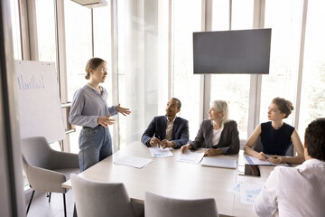 Young woman coach stands in front of company clients, investors or colleagues make flip chart...