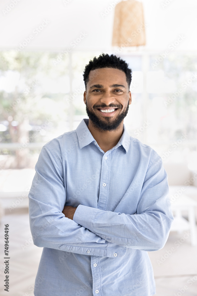 Wall mural happy handsome young african american entrepreneur man in office shirt standing indoors with crossed