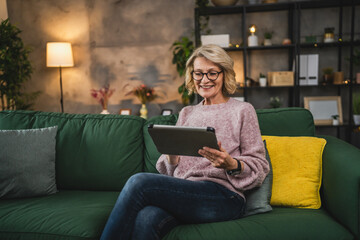 Obraz premium mature blonde woman with eyeglasses use digital tablet at home
