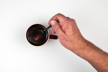 Caucasian male hand stirring coffee in brown cup with metal spoon on white background