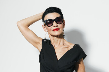 Stylish woman in black dress and sunglasses posing with hands on head for camera portrait