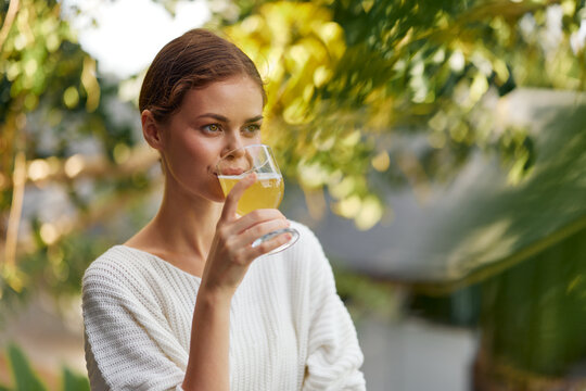 Happy Woman Enjoying a Refreshing Kombucha Drink in the Sunlight, Surrounded by Nature and Holding a Glass of Antioxidantrich Detoxing Beverage