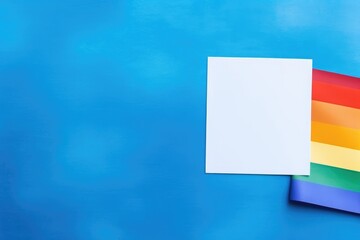 Blank Card with Rainbow Pride Flag on Blue Background. A vibrant rainbow flag partially covered by a blank white card, presented on a striking blue backdrop for messages of LGBTQ+ support and pride.