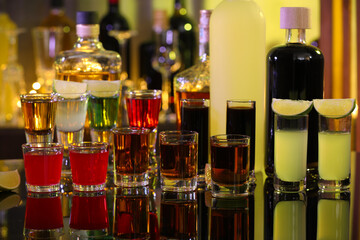 Different shooters in shot glasses and bottles on mirror surface. Alcohol drink