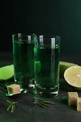 Absinthe in shot glasses, spoon, brown sugar, lime and rosemary on gray table. Alcoholic drink